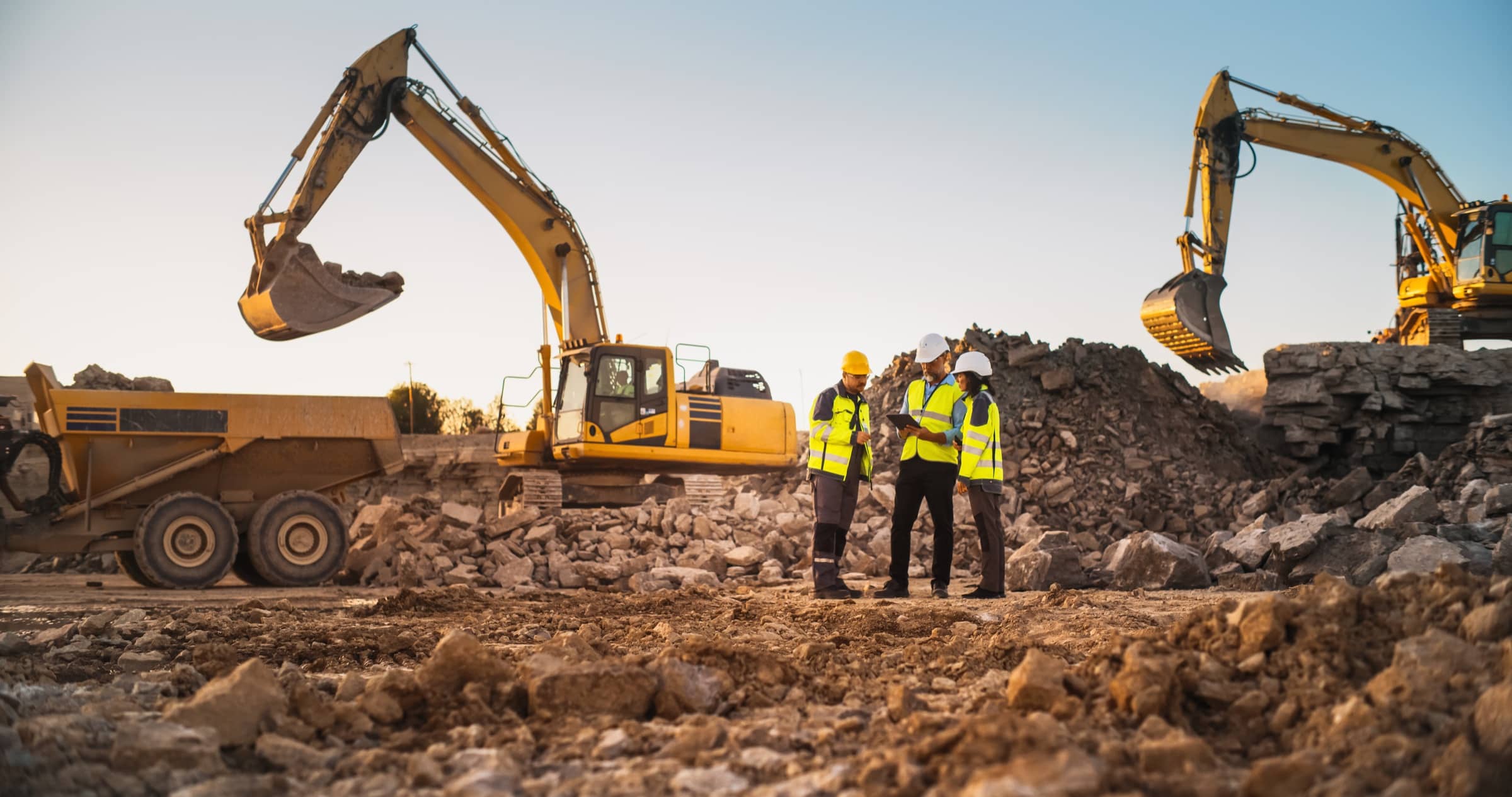 Crew reviewing a tablet on a quarry site between two excavators